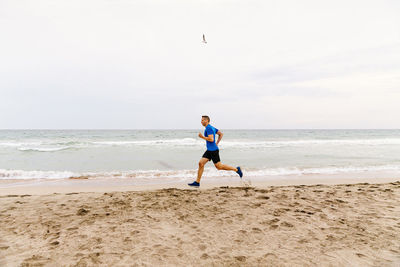 Full length of man running on beach against sky