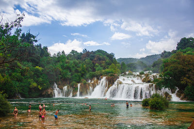 Panoramic view of people by waterfall against sky