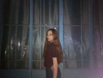 Woman looking away while standing against window