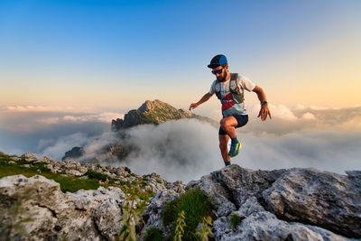 Rear view of man climbing on rock against sky during sunset