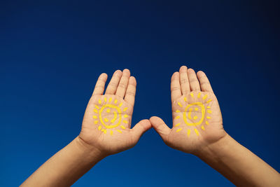 Cropped image of painted hands against blue sky