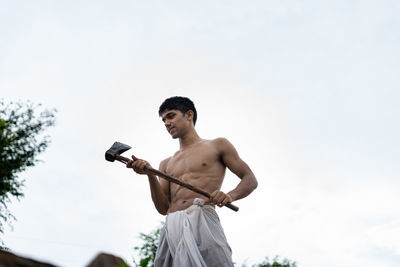 Low angle view of shirtless man holding camera against sky