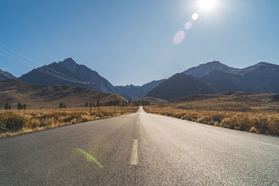 Empty desert road leading to mountains against clear blue sky