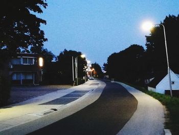 Street amidst illuminated city against sky at dusk