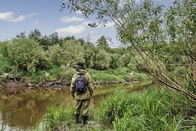 Active male in protective suit with backpack standing near taiga river in a siberian forest, russia.