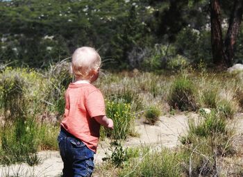 Side view of baby boy standing on field in forest