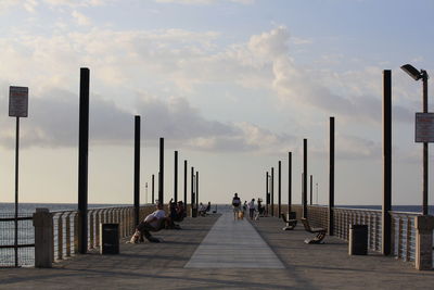 People walking on footpath by street against sky