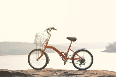 Bicycle on rock by river against clear sky