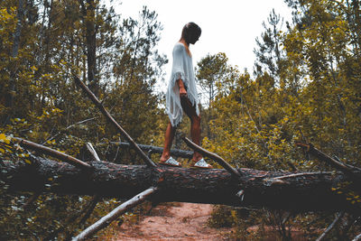 Side view of young woman walking on fallen tree in forest