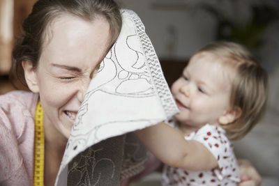 Cheerful fashion designer and daughter playing with cloth at home