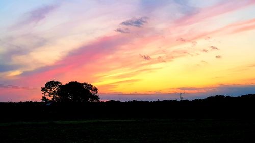 Silhouette trees on field against romantic sky at sunset