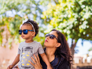 Mother and daughter wearing sunglasses against trees at park