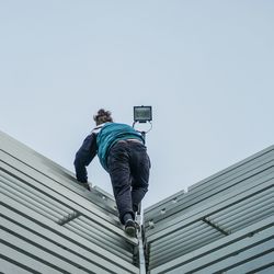 Low angle view of teenage boy standing on fence against sky