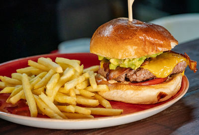 A close up image of a guacamole and bacon filled beef burger served with french fries