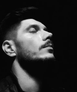 Portrait of young man looking away against black background