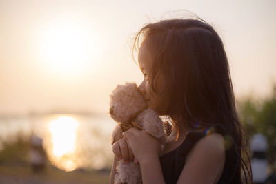 Smiling girl looking away while holding stuffed toy against sky