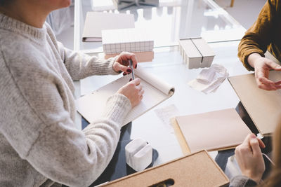 High angle view of female design professional with note pad discussing with colleagues at desk in workshop