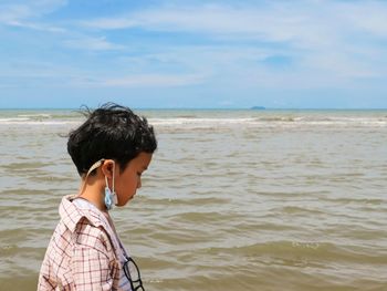 Rear view of boy on beach against sky