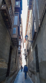 Rear view of people walking on narrow alley amidst buildings in city