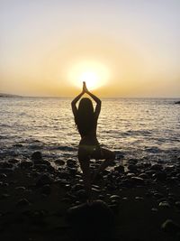 Rear view of woman doing tree pose at beach during sunset
