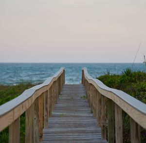 Wooden bridge over sea against clear sky