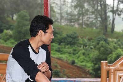 Young man looking away against trees in forest