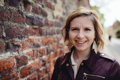 Portrait of smiling young woman by brick wall