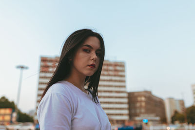 Low angle view portrait of young woman standing in city against sky