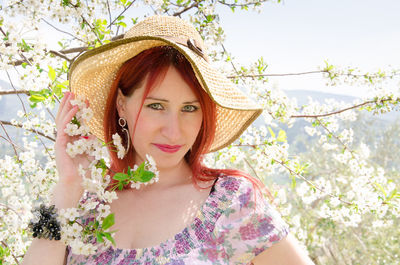 Portrait of woman wearing hat by blooming flowers