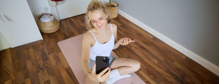 Full length of young woman sitting on hardwood floor at home