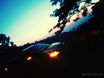 Cars on illuminated street against sky at sunset