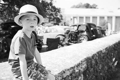 Portrait of cute boy wearing hat while sitting on retaining wall