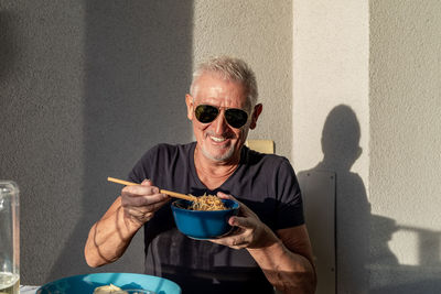 Attractive middle-aged man have fun while eating sitting on table laid chinese food in front of wall