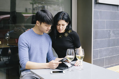 Couple using digital tablet while sitting at sidewalk cafe