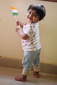 Portrait of smiling girl holding flag while standing against wall