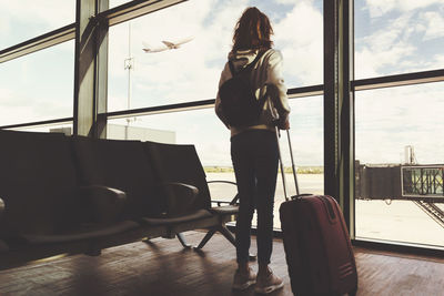 Rear view of girl with luggage standing in waiting room