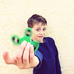 Portrait of boy playing with green fidget spinner against wall