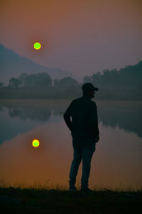 Rear view of man standing on field against sky during sunset