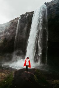 Woman standing on rock against waterfall