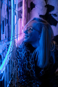 Smiling young woman by illuminated lighting equipment on fence