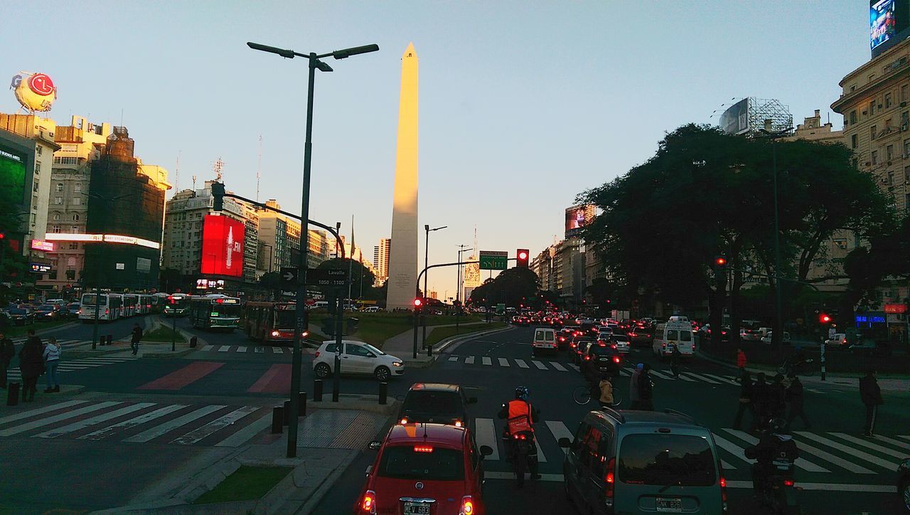 transportation, car, land vehicle, mode of transport, building exterior, clear sky, street, architecture, road, traffic, built structure, city, street light, city street, sky, road marking, tree, city life, copy space, dusk