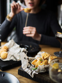 Cropped unrecognizable woman eating delicious deep fried dumplings garnished with green herbs placed on paper served with white sauce on wooden table