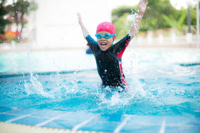 Portrait of cheerful girl splashing water in swimming pool