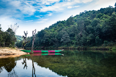 Isolated wood boat with water refection at calm river surrounded by dense green forests at morning