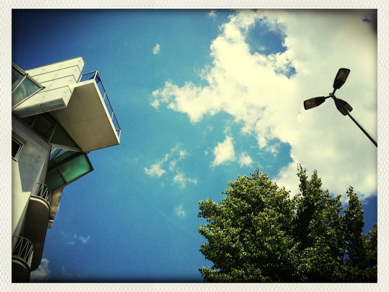 low angle view, sky, building exterior, built structure, architecture, street light, transfer print, auto post production filter, cloud - sky, cloud, tree, blue, day, outdoors, lighting equipment, building, high section, no people, cloudy, house