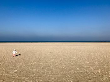 Child walking at beach against clear blue sky