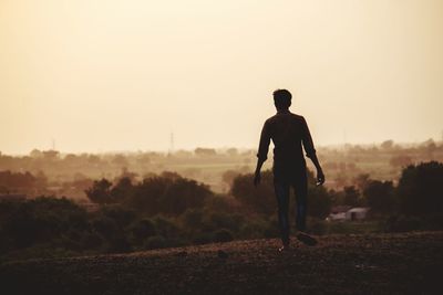 Rear view of silhouette man walking on field against sky