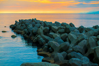 Rocks on sea shore against sky during sunset