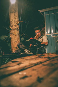 Full length of man using mobile phone while sitting on wood