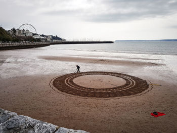 Man drawing on beach against sky